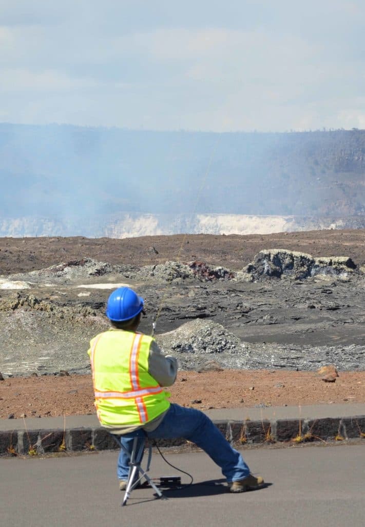 Man in bright safety vest flying a kite near a volcano giving off gas